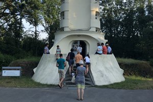 Frontalansicht. Menschen, die an einem sonnigen Tag im Eingangsbereich des Einsteinturms auf einer Mauer sitzen oder gerade hineingehen.