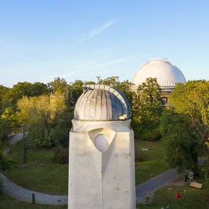 Blick auf die Rückseite des Einsteinturms, im Hintergrund die Kuppel des Großen Refraktors. Dazwischen Bäume und Wiese.