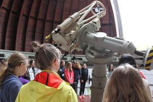 Students, who stand around a smaller reflecting telescope inside a wooden dome with an opened slit.