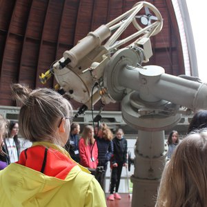 Students, who stand around a smaller reflecting telescope inside a wooden dome with an opened slit.