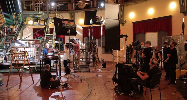 On the right is the filming team with camera and director. On the left, Harald Lesch stands in the centre, around him the light and camera are adjusted. One end of the refractor is visible in the background.