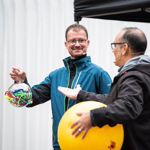 Zwei Wissenschaftler, einer hält einen Sonnenball unter dem Arm und erklärt etwas, der andere hält ein Modell der Sonne mit den Magnetfeldlinien in der Hand