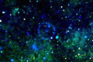 X-ray image with point sources in shades of blue and green against a dark background. A blue ring is visible in the centre around a blue point source.