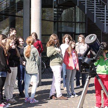 Several girls at a small telescope with a solar filter. One girl is just looking through the telescope.