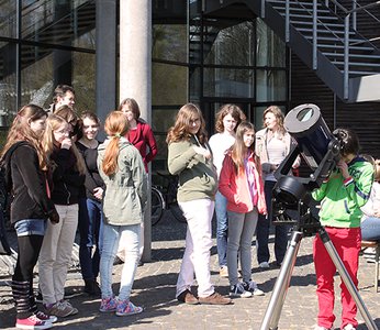 Several girls at a small telescope with a solar filter. One girl is just looking through the telescope.