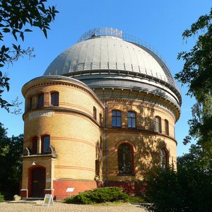 The Great Refractor from the outside on a sunny day. Side view. The slit of the white dome is opened, the trees cast shadows on the clinker brick building.